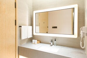 A modern bathroom with a large mirror, a sink, a towel rack, and a hairdryer. - Jinjiang Inn Style (Fuzhou)