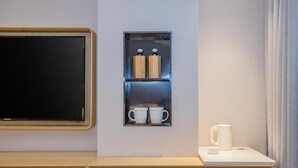 A modern hotel room with a wooden desk, a built-in shelf with two bottles and two cups, and a coffee maker on a small table. - Jinjiang Inn Style (Fuzhou)