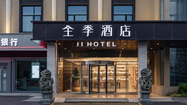 A hotel entrance with a revolving door, stone lion statues, and a sign reading "JI HOTEL". - Jinjiang Inn Style (Fuzhou)