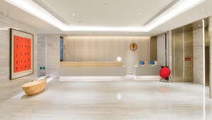A modern hotel lobby with a reception desk, a wooden seating area, and a digital information kiosk. - Jinjiang Inn Style (Fuzhou)