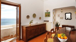 A dining area with a view of the sea, a wooden buffet, and a table with a bowl of fruit.