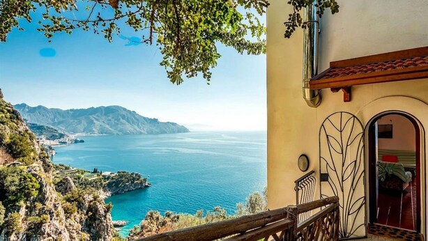 A coastal view with a wooden staircase leading to a building with a tiled roof and a metal gate.