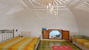A bedroom with a bed, a sofa, a TV, and a view of the sea.