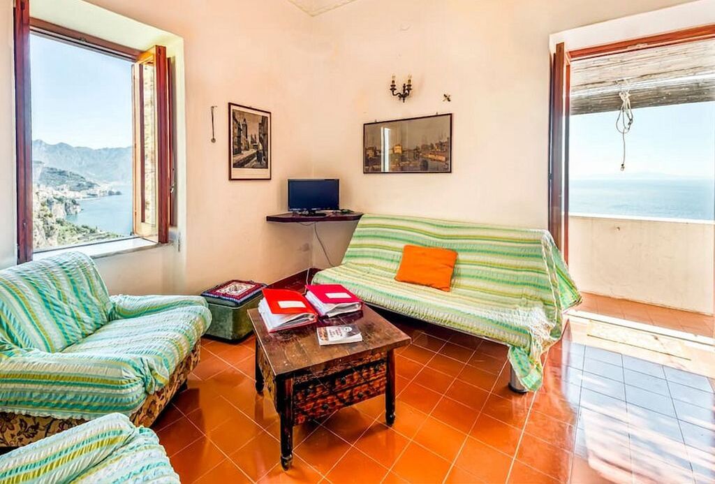 Una habitación con vistas al mar, un sofá, una pequeña mesa con libros y un escritorio con una computadora.
