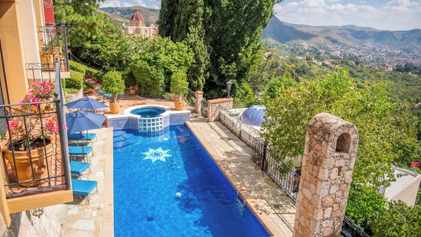 A swimming pool with a sun design, surrounded by stone walls and potted plants, overlooking a scenic landscape. - Casa Estrella Valenciana Hotel Boutique (Guanajuato)