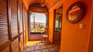 A narrow hallway with wooden doors, a patterned rug, a chair, and a view of a building through a window. - Casa Estrella Valenciana Hotel Boutique (Guanajuato)