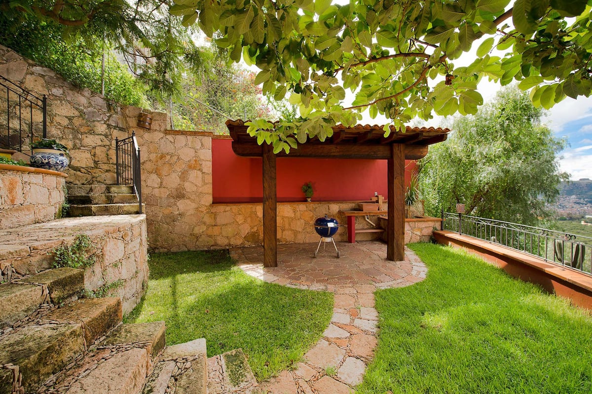 A stone staircase leading to a red wall with a wooden pergola and a barbecue grill.