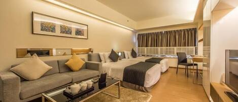 A modern hotel room with a sofa, two single beds, a desk, and a TV.