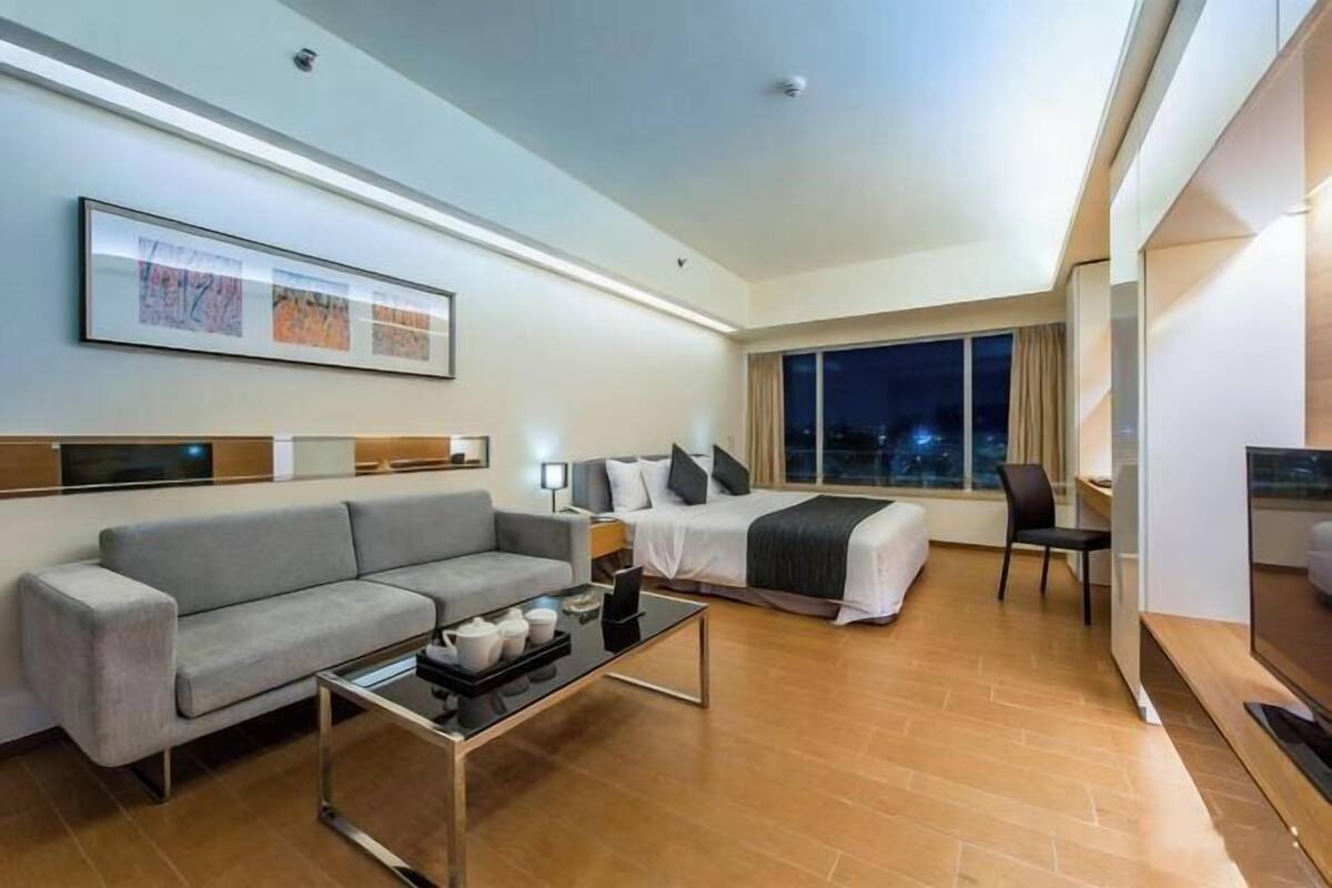A modern hotel room with a sofa, a bed, a desk, and a TV.