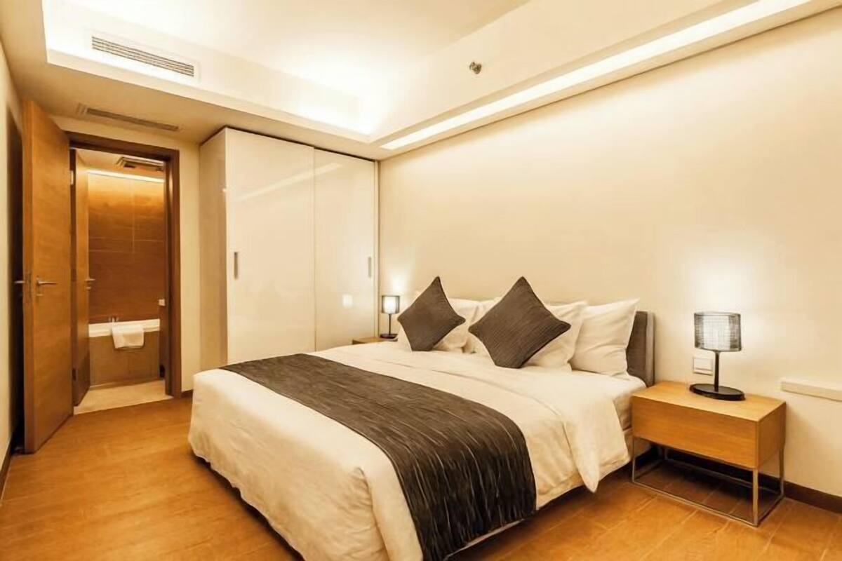 A modern hotel room with a large bed, a bedside table with a lamp, and a wardrobe.