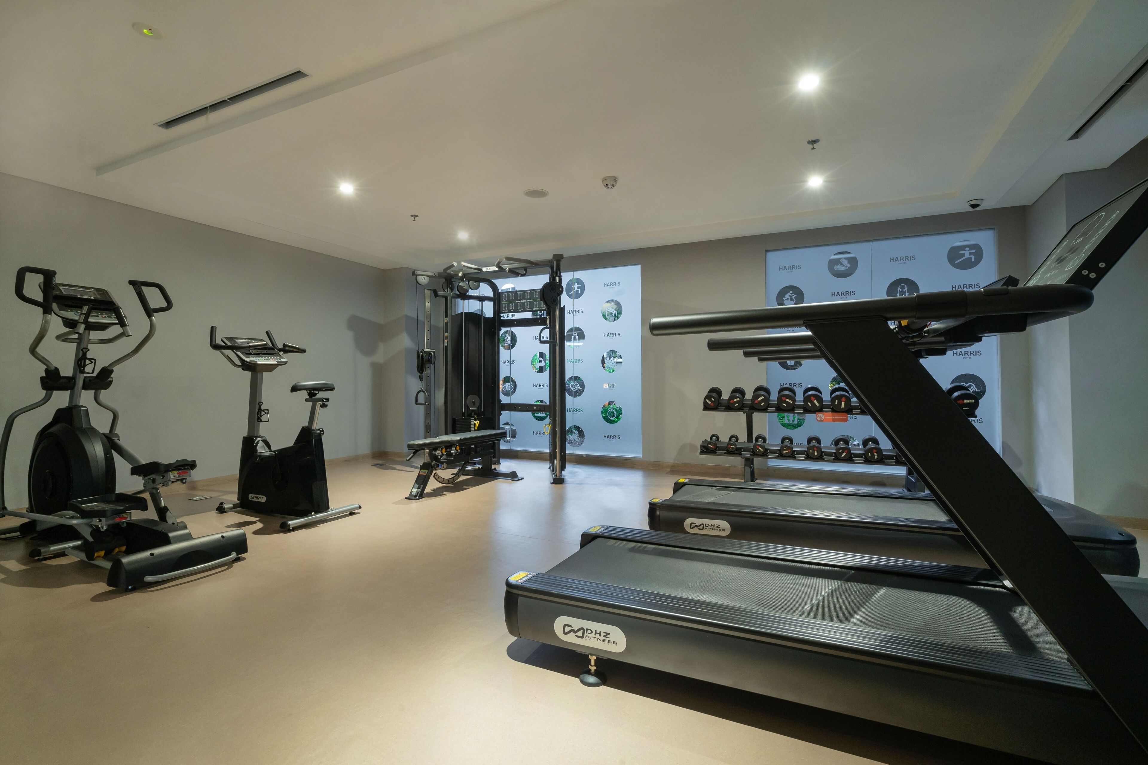 Een moderne sportschool met cardioapparatuur, krachtstations en een muur met fitnesspictogrammen.