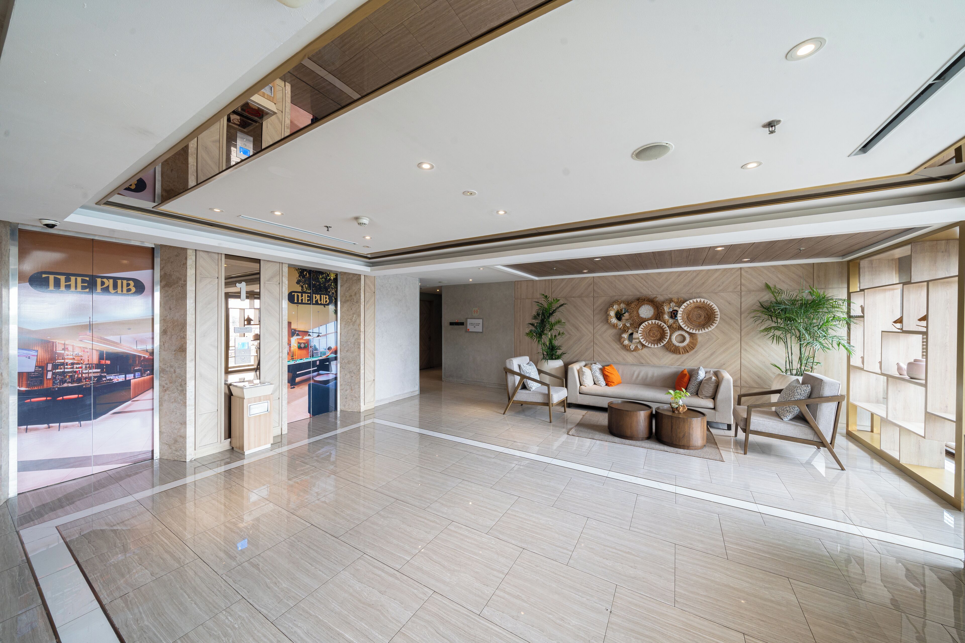 Un hall d’entrée spacieux au design moderne, comprenant un espace de réception, un coin salon avec des canapés et une table basse, et offrant une vue sur le restaurant « The Pub ».