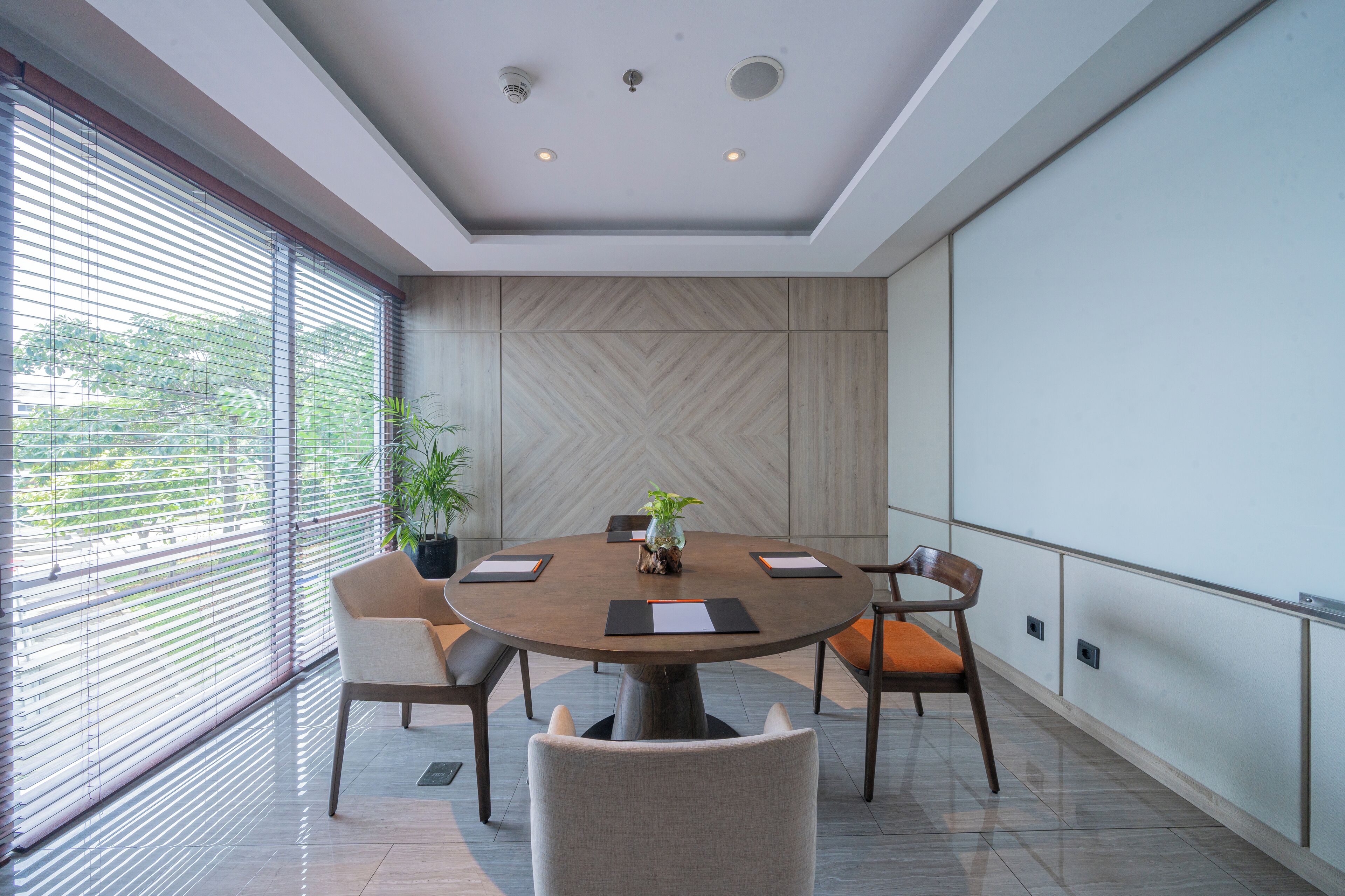 A modern conference room with a round table, six chairs, and a projector screen.