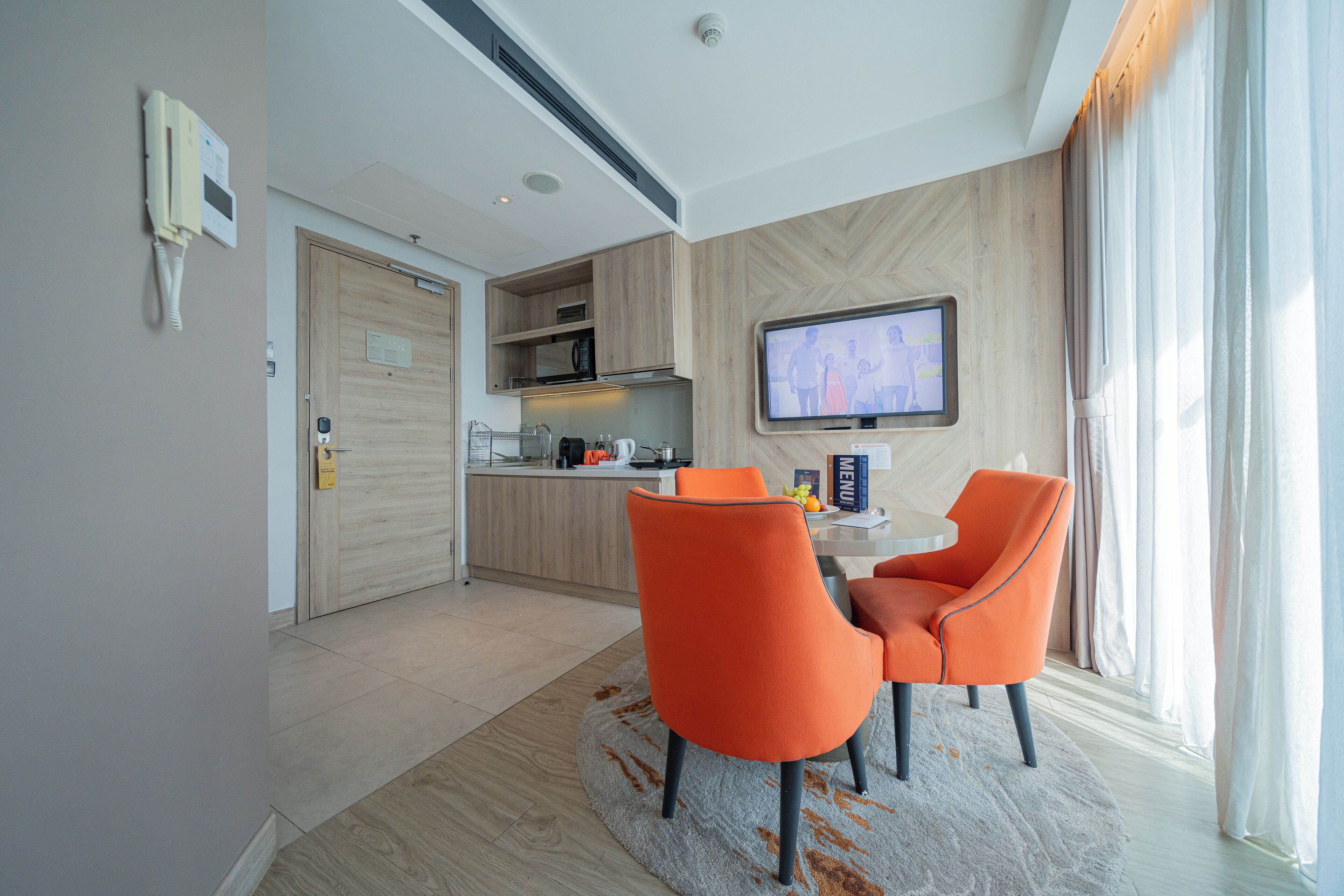 A modern hotel room with a dining area, a kitchen, and a TV.