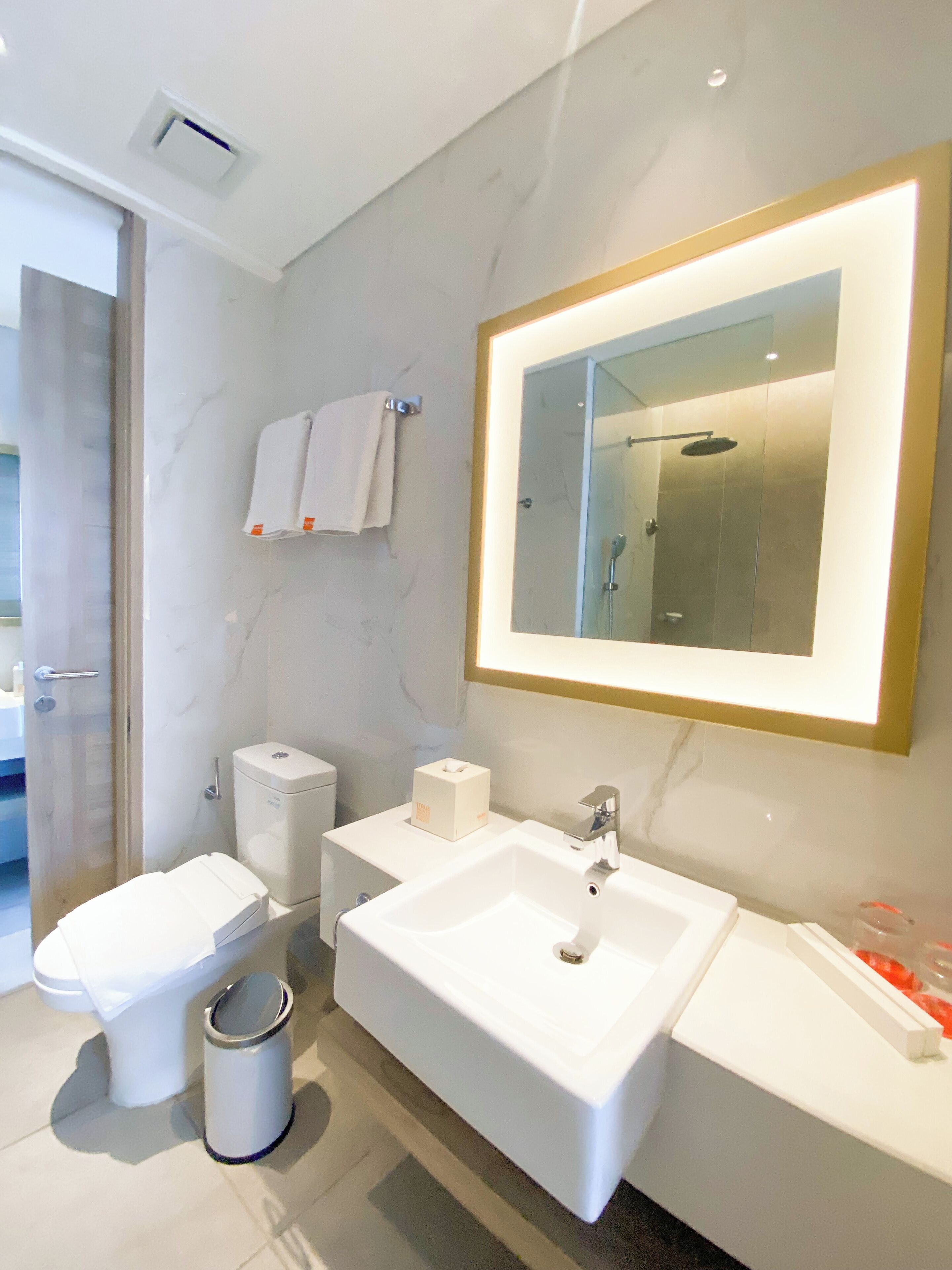 A modern bathroom with a white sink, a toilet, a bidet, and a mirror with a gold frame.