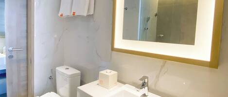 A modern bathroom with a white sink, a toilet, a bidet, and a mirror with a gold frame.