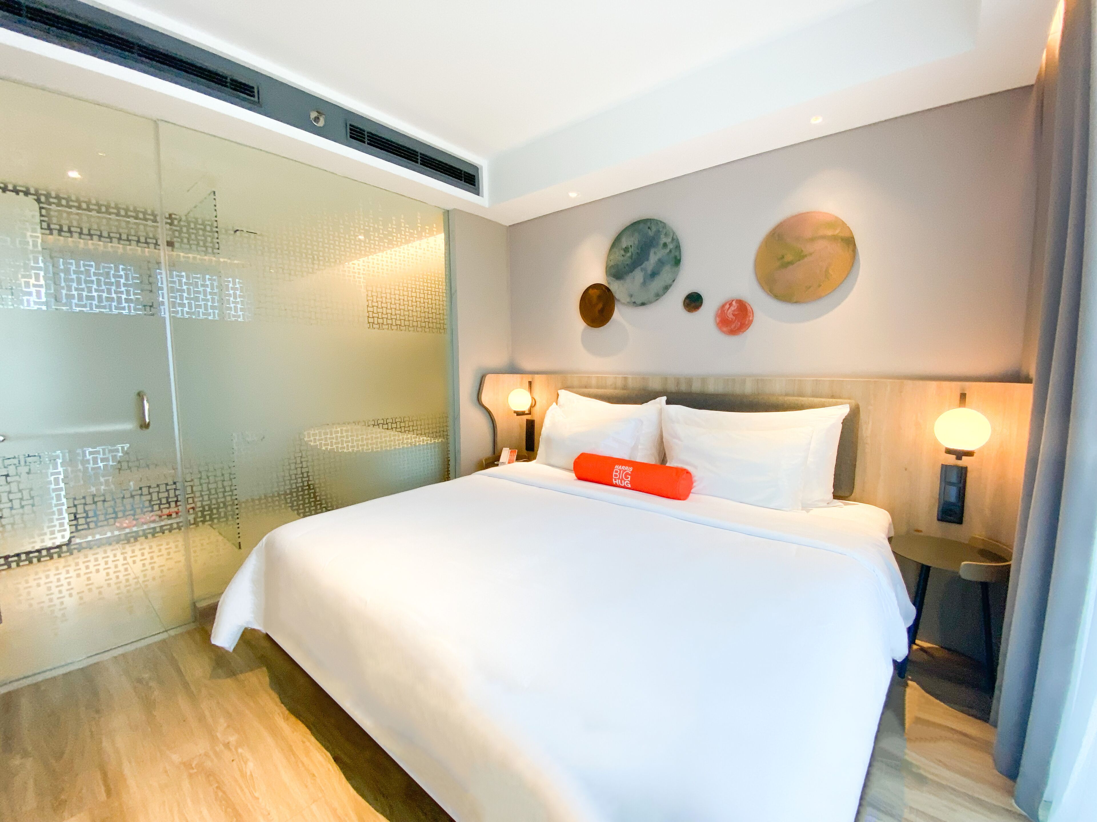 A modern hotel room with a large bed, a glass-enclosed shower, and decorative wall art.
