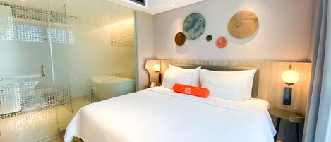 A modern hotel room with a large bed, a glass-enclosed shower, and decorative wall art.