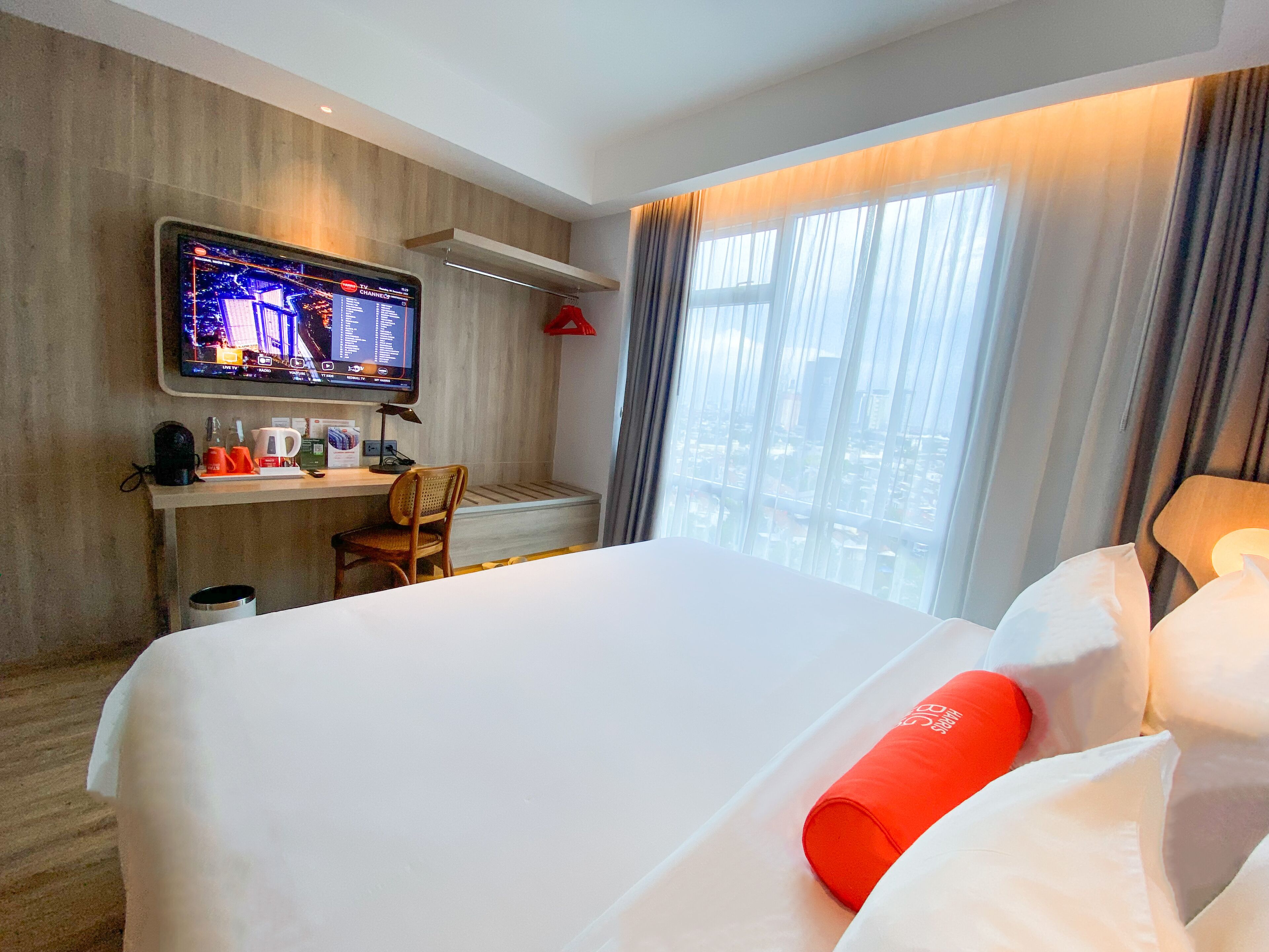 Une chambre d’hôtel avec un lit, un bureau avec un ordinateur, un téléviseur fixé au mur et une fenêtre avec des rideaux.