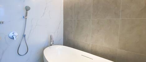 Ein modernes Badezimmer mit einer freistehenden Badewanne, einer Handbrause und einer wandmontierten Bedienkonsole.