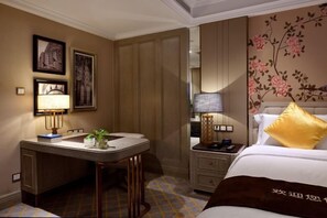 A hotel room with a bed, bedside table, lamp, and a desk with a chair.