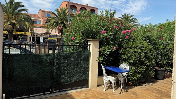 A patio area with a table and chairs, a gate, and a building with a restaurant sign in the background.