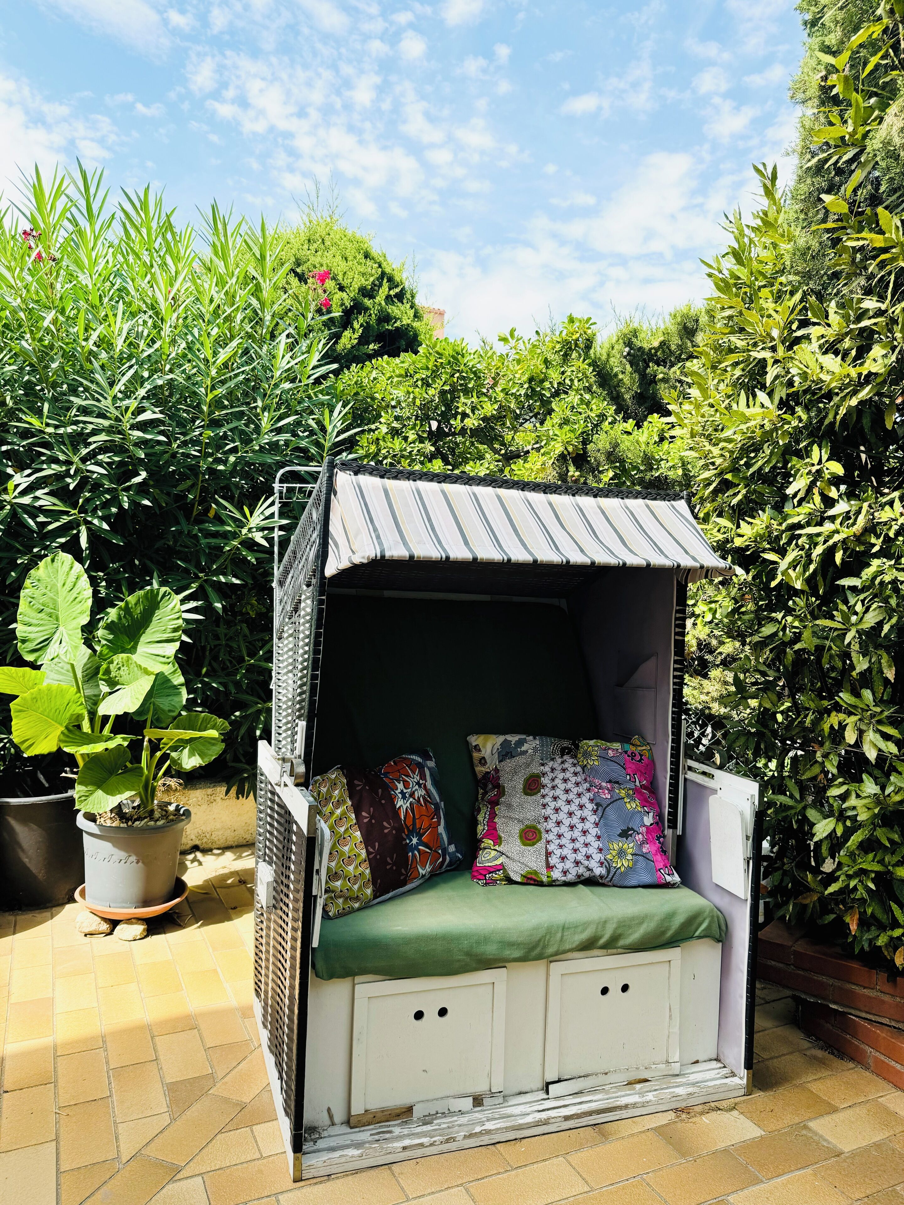 Um balanço de jardim com toldo listrado, almofadas verdes e assento branco.