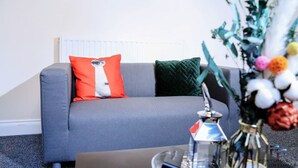 A grey sofa with two pillows, one red and one green, and a vase with flowers in a living room. - Beautiful 5-bed House Roker Beach (Sunderland)