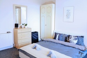 Une chambre à coucher comprenant un lit, une commode, une armoire, un miroir et un mur orné d’une citation inspirante.