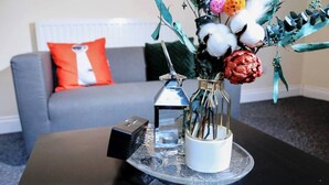 A modern living room with a grey sofa, a red and white pillow, and a coffee table with a decorative vase and a small lantern. - Beautiful 5-bed House Roker Beach (Sunderland)