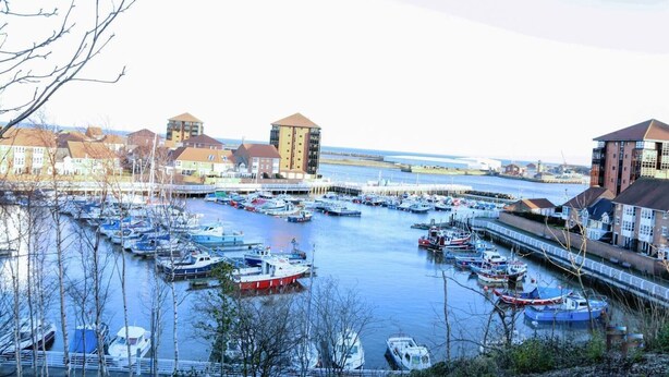 A marina with numerous boats docked, surrounded by buildings with distinct architectural styles. - Beautiful 5-bed House Roker Beach (Sunderland)
