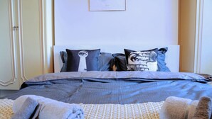 A neatly made bed with a patterned bedspread, two pillows with a skull design, and rolled towels on the floor. - Beautiful 5-bed House Roker Beach (Sunderland)