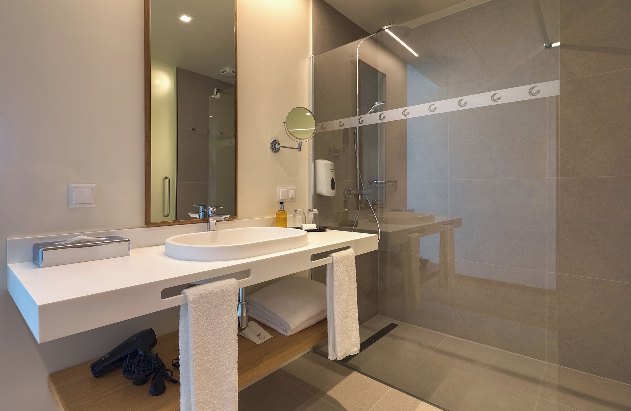 Un baño moderno con un espejo grande, un lavabo y una ducha con mampara de vidrio.