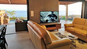 Un salon doté d’un grand téléviseur à écran plat, de canapés en cuir, d’une table basse et offrant une vue sur l’océan.