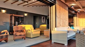 Un salon moderne avec un canapé, des fauteuils et un téléviseur. Le plafond est en bois et il y a une grande fenêtre.