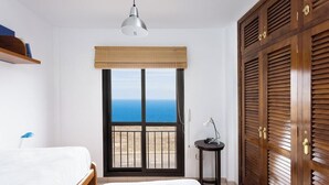 Un dormitorio con cama, mesita de noche, lámpara, armario y ventana con vista al mar.
