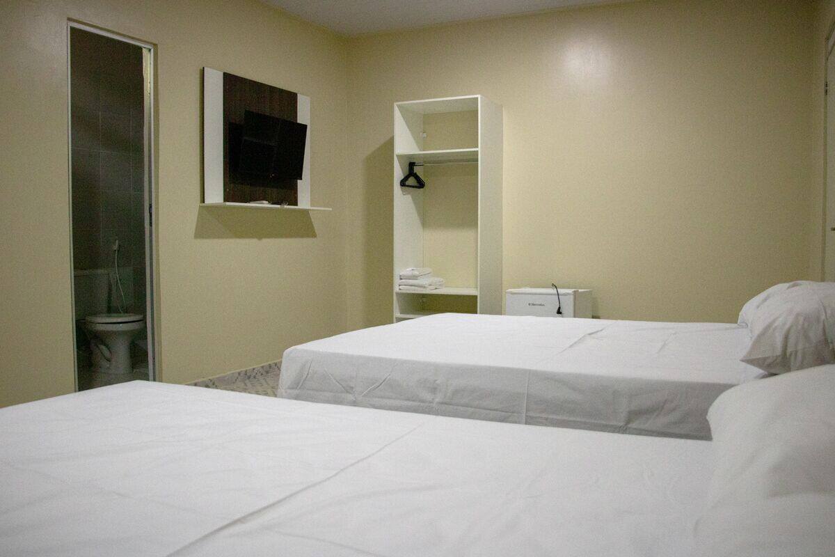 A hotel room with two beds, a bathroom with a toilet, a mirror, and a TV mounted on the wall.