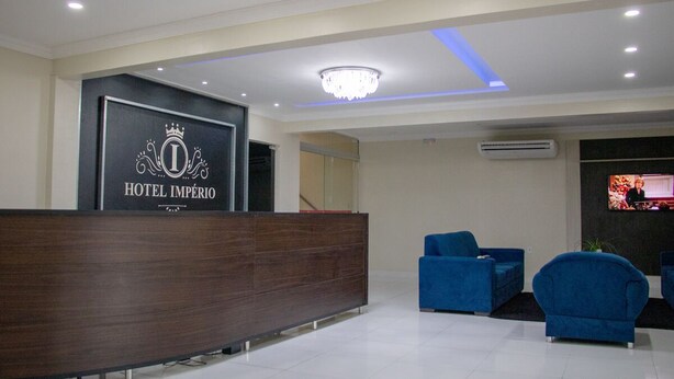A hotel reception area with a reception desk, blue armchairs, and a chandelier. - Hotel Império (Santarém)