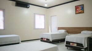 A hotel room with three single beds, a window, an air conditioning unit, and a door. - Hotel Império (Santarém)