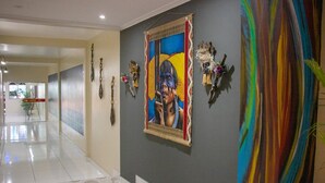 A hallway with a tiled floor, a large painting on the wall, and several decorative items including masks and a colorful abstract painting. - Hotel Império (Santarém)