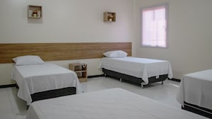 A hotel room with three single beds, a wooden headboard, a bedside table with a lamp, and a window with blinds. - Hotel Império (Santarém)