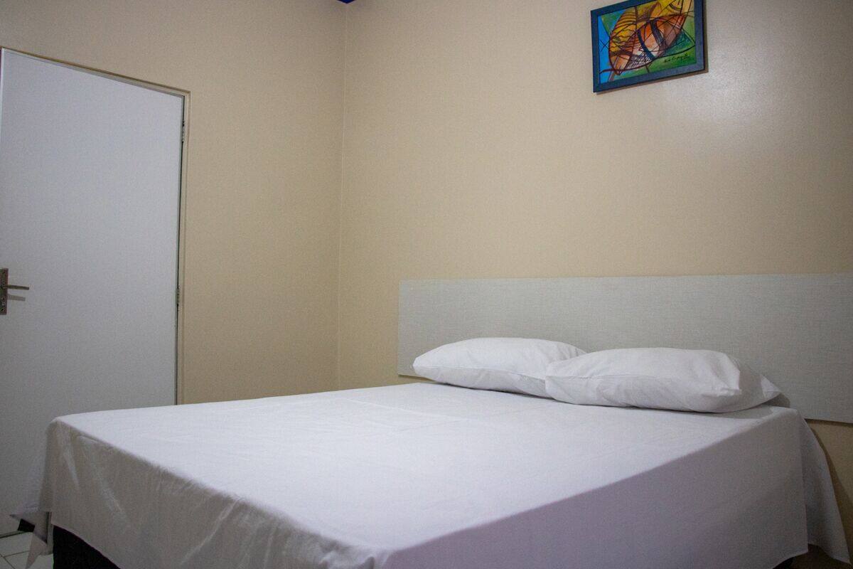 A single bed with white bedding in a room with a plain wall and a door.