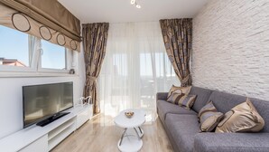 Ein modernes Wohnzimmer mit Fernseher, einem weißen Couchtisch und einem grauen Sofa mit gemusterten Kissen.
