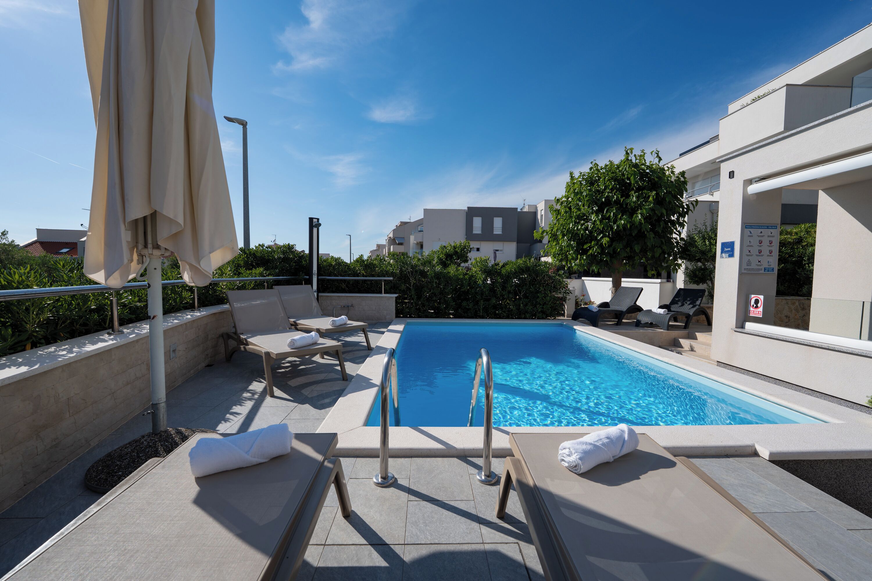 Un espace piscine sur le toit, avec des chaises longues, un escalier pour accéder à la piscine et un ciel d’un bleu limpide.