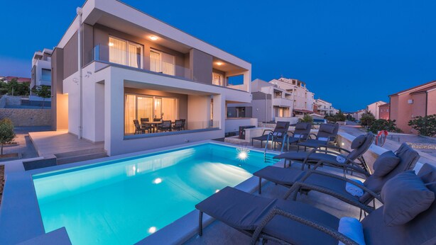 Ein modernes, zweistöckiges Gebäude mit Swimmingpool und Liegestühlen.
