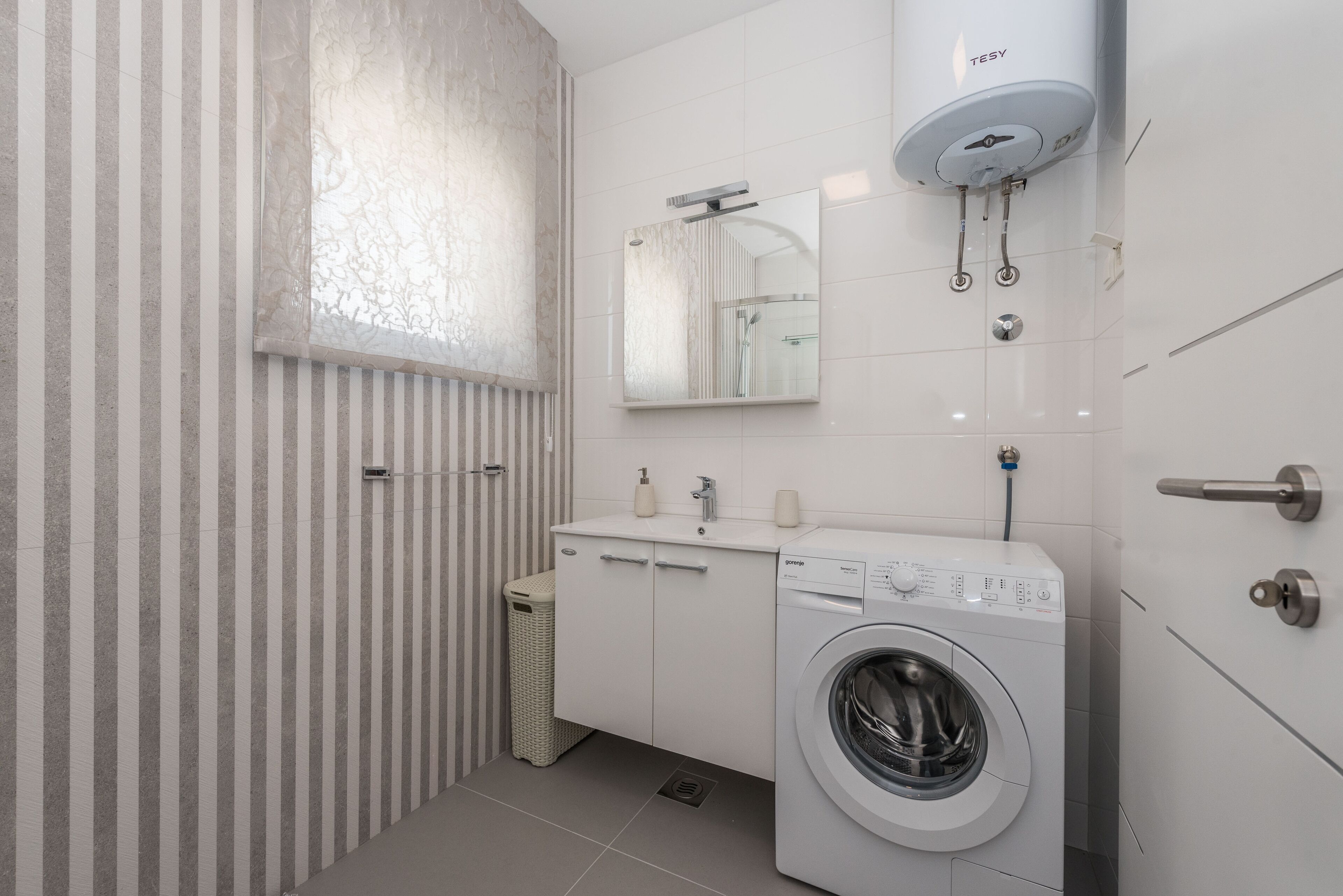 Un baño moderno con pared a rayas, lavadora integrada y zona de ducha.