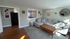 A living room with a grey sectional sofa, a wooden coffee table, and a grey rug. There is a window providing natural light and a door leading to another room. - Close to Pier and Downtown | Everything Included | Relax & Enjoy (Old Orchard Beach)