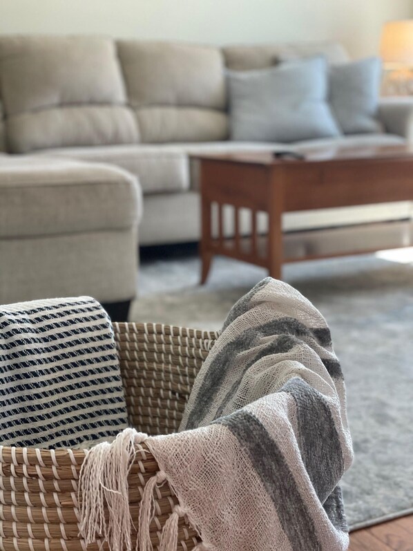 A living room with a beige sofa, a wooden coffee table, and a woven basket with a striped blanket.