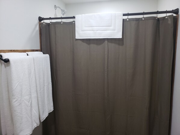 Un baño con cortina de ducha, un perchero con dos toallas blancas y un cabezal de ducha.