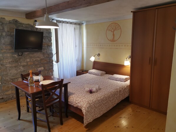 A bedroom with a wooden bed, a desk with a chair, a television mounted on a stone wall, and a wooden wardrobe. - TIERRA - Apartments Bevk in charming Piran (4 Piran)